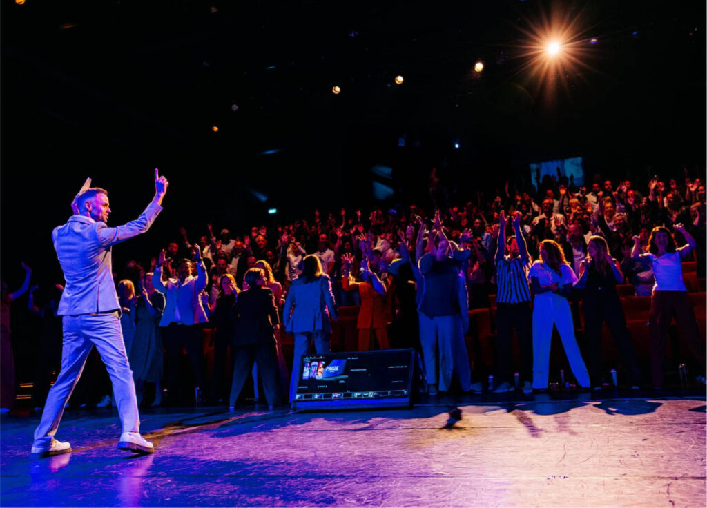 Dagvoorzitter Marc Neerhof met een enthousiaste zaal met handen in de lucht